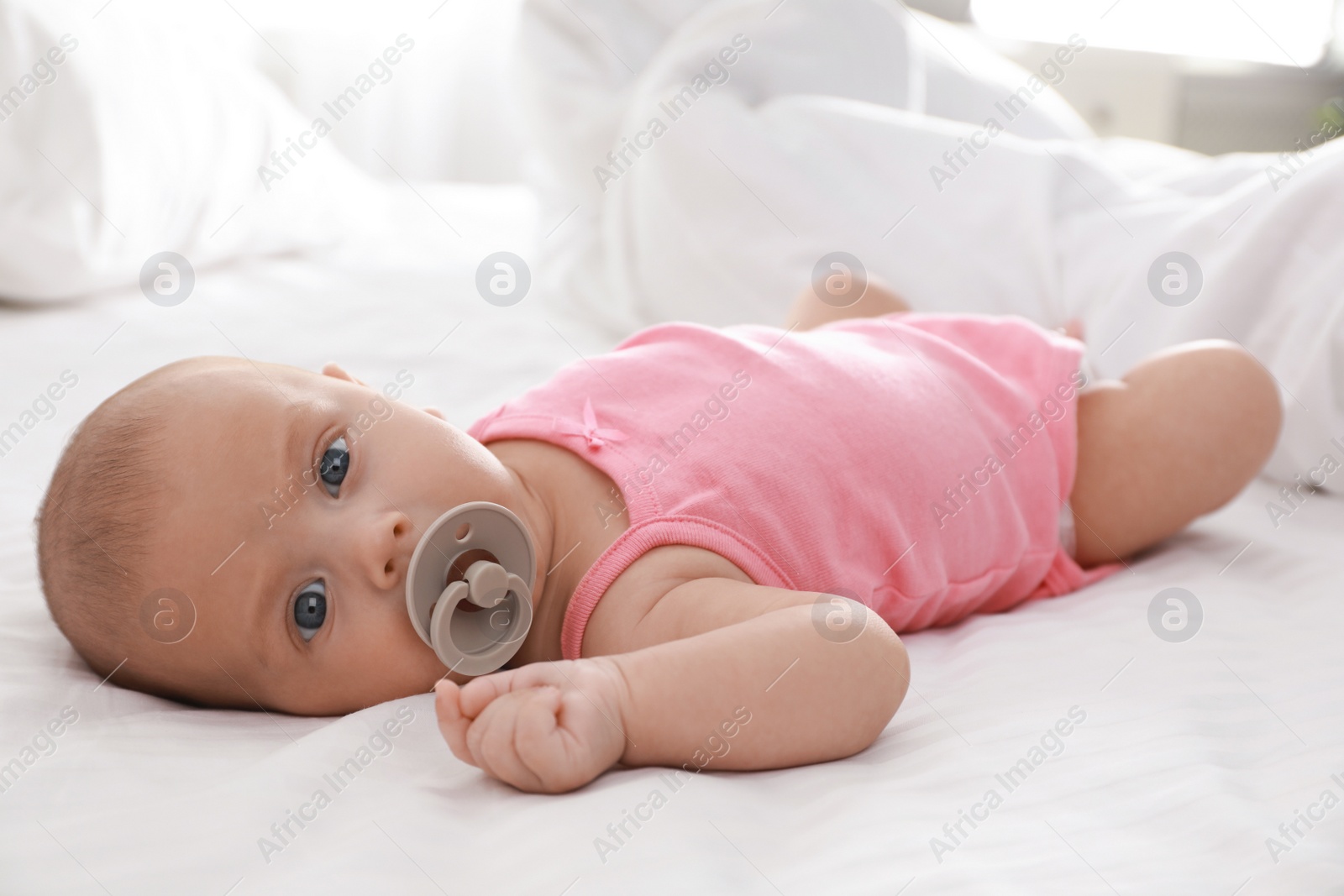 Photo of Cute little baby with pacifier lying on bed