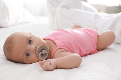 Cute little baby with pacifier lying on bed