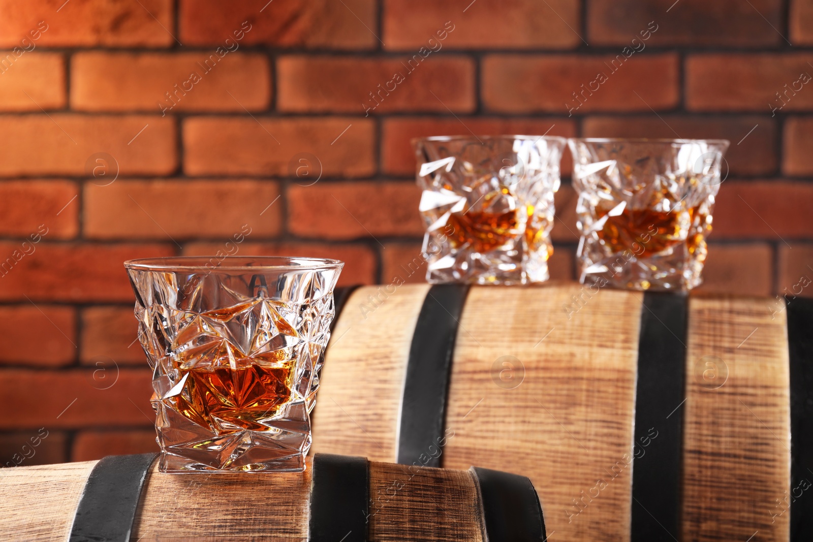 Photo of Glasses of whiskey on wooden barrels against brick wall