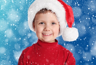 Cute child in Santa hat under snowfall on blue background. Christmas celebration