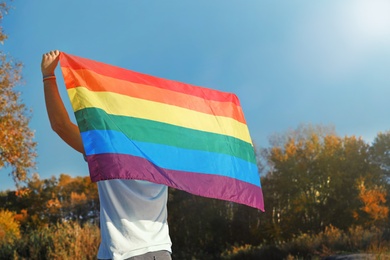 Photo of Man with rainbow LGBT flag outdoors, space for text. Gay symbol