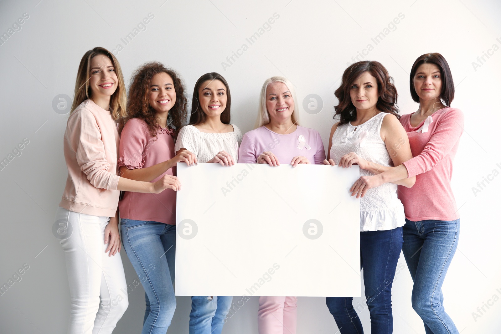 Photo of Women wearing silk ribbons holding poster with space for text against white background. Breast cancer awareness concept