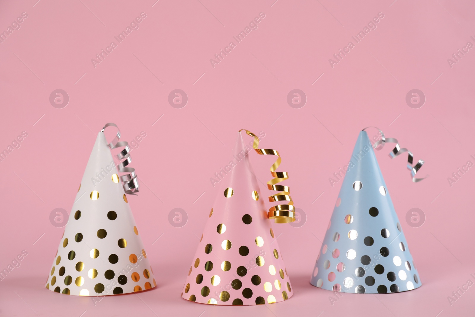 Photo of Bright party hats with streamers on pink background