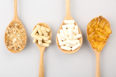 Photo of Wooden spoons with different vitamin capsules on light grey background, flat lay