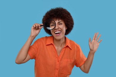 Photo of Excited woman looking through magnifier glass on light blue background