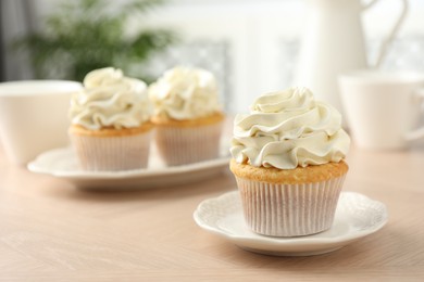 Tasty cupcakes with vanilla cream on light wooden table, closeup