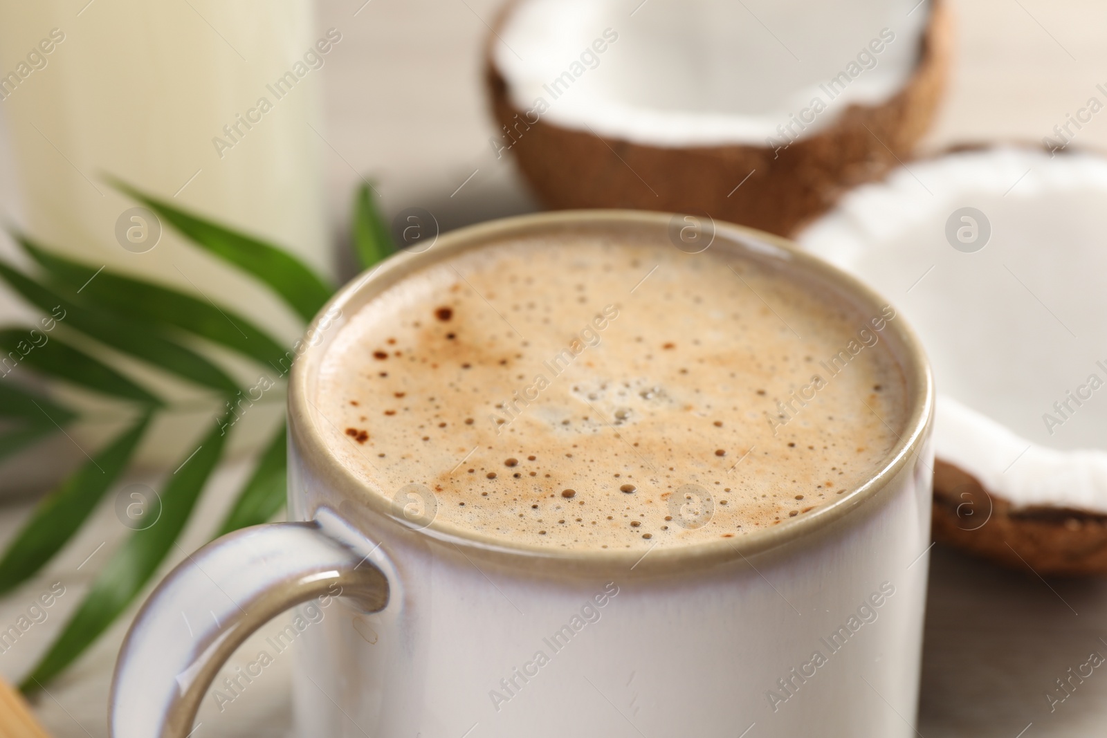 Photo of Cup of coffee, halves of coconut and green leaves on table, closeup