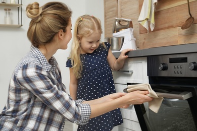 Photo of Mother and her daughter baking food in oven at home