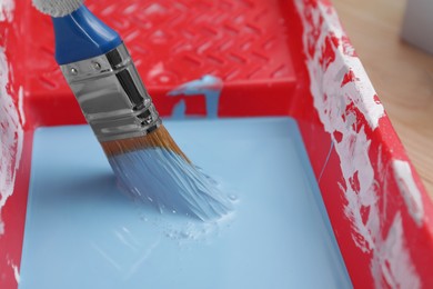Photo of Tray with light blue paint and brush on table, closeup