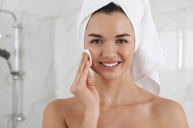 Photo of Beautiful young woman with hair wrapped in towel cleaning her face indoors