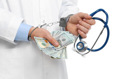 Photo of Doctor in handcuffs with bribe and stethoscope on white background, closeup. Corrupted medicine