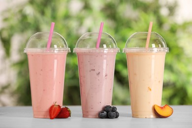 Photo of Plastic cups with different tasty smoothies and fresh fruits on wooden table outdoors