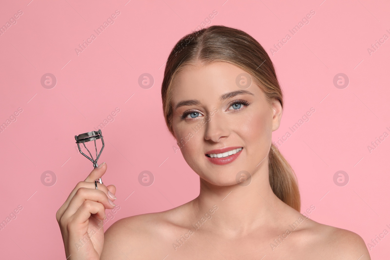 Photo of Young woman with eyelash curler on pink background