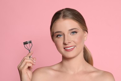 Young woman with eyelash curler on pink background