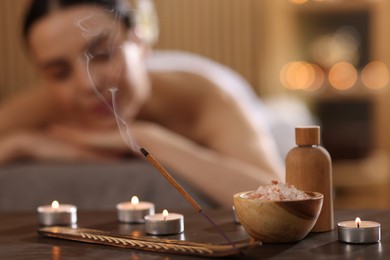 Photo of Spa therapy. Beautiful young woman lying on massage table in salon, focus on burning candles, salt and incense stick