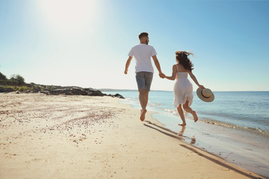 Photo of Young couple running on beach near sea. Honeymoon trip