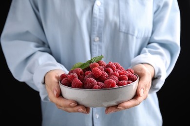 Photo of Woman holding bowl with fresh ripe raspberries against black background, closeup