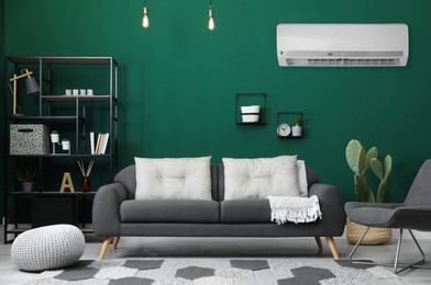 Modern air conditioner on green wall in living room with stylish furniture
