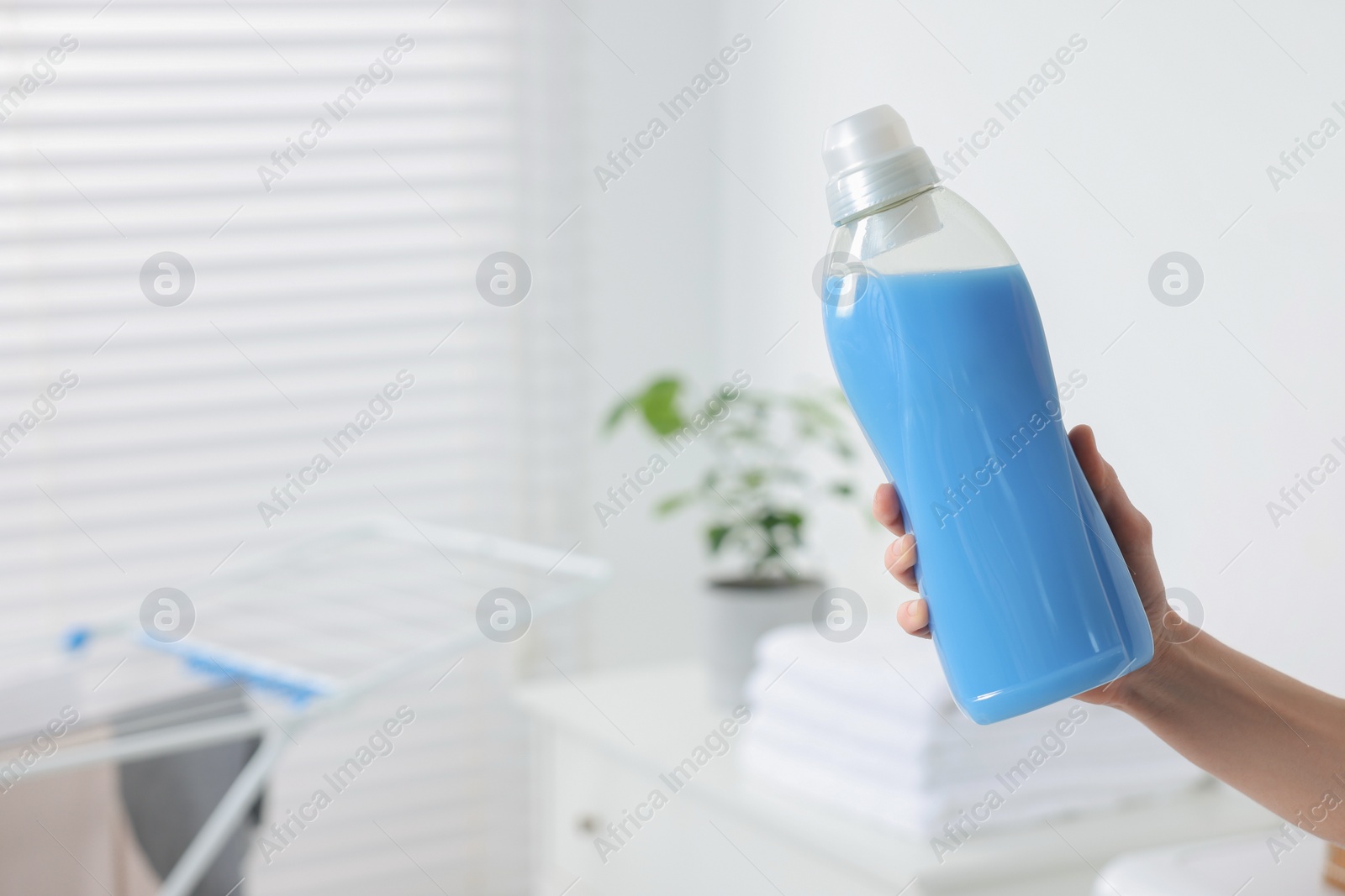 Photo of Woman holding fabric softener in bathroom, closeup. Space for text