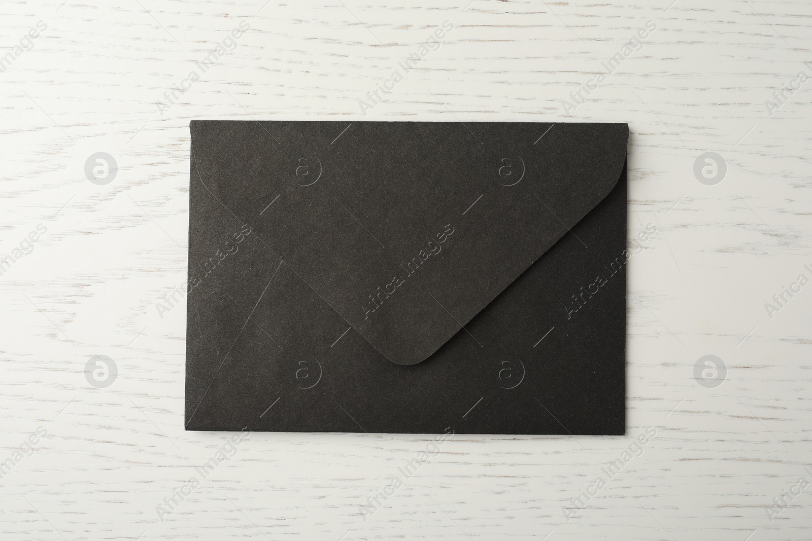 Photo of Black paper envelope on white wooden background, top view