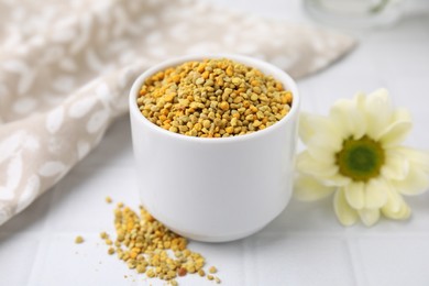 Photo of Fresh bee pollen granules and flower on white tiled table, closeup
