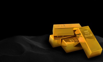 Image of Shiny gold bars on black sand, space for text