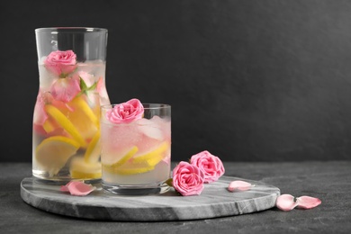 Photo of Delicious refreshing drink with lemon and roses on table against grey background. Space for text