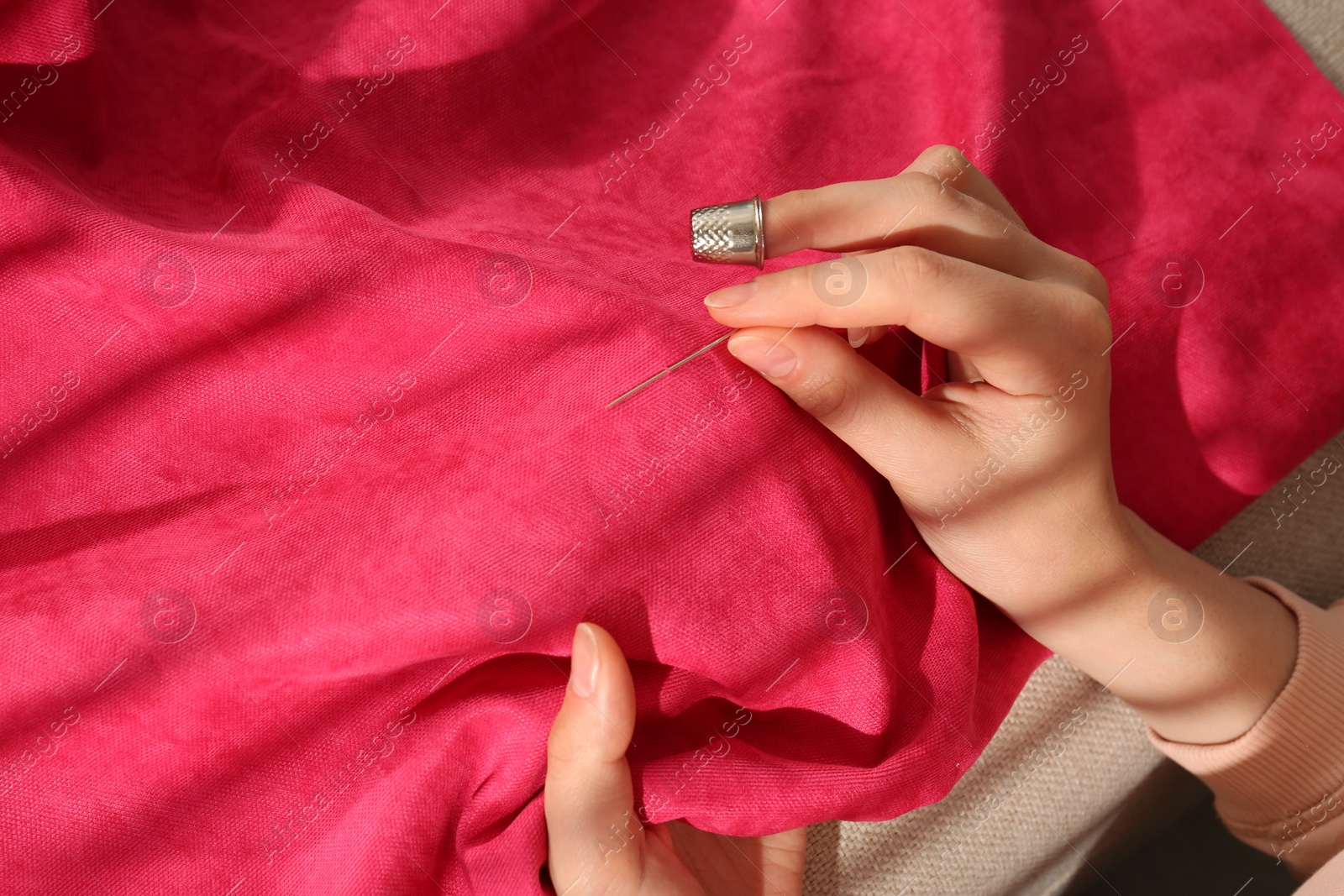 Photo of Woman sewing on red fabric with thimble and needle, closeup