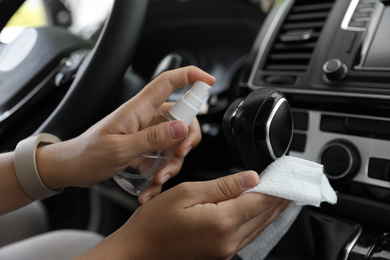 Photo of Woman cleaning gear stick with wet wipe and antibacterial spray in car, closeup