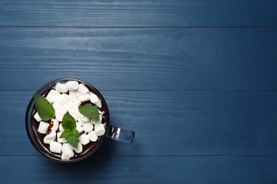 Glass cup of delicious hot chocolate with marshmallows and fresh mint on blue wooden table, top view. Space for text