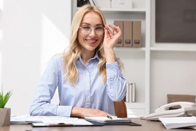 Photo of Happy secretary at table with stationery in office