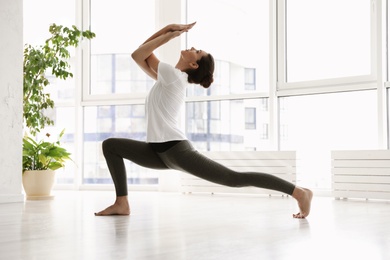 Photo of Young woman practicing crescent lunge pose with eagle arms in yoga studio