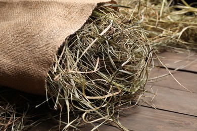 Burlap sack with dried hay on wooden table, closeup