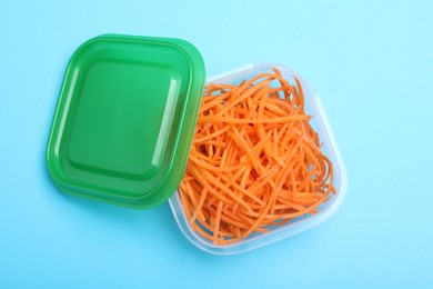 Fresh shredded carrots in glass container on light blue background, top view