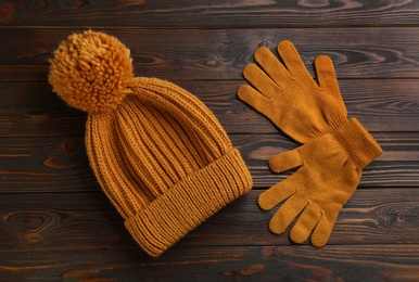 Woolen gloves and hat on wooden background, flat lay