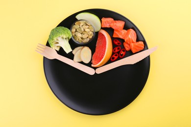 Photo of Metabolism. Plate with different food products and wooden cutlery on pale yellow background, top view