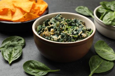 Photo of Tasty spinach dip with egg in bowl and nachos chips on black table, closeup