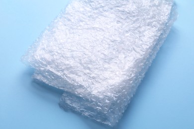 Photo of Folded transparent bubble wrap on light blue background, closeup