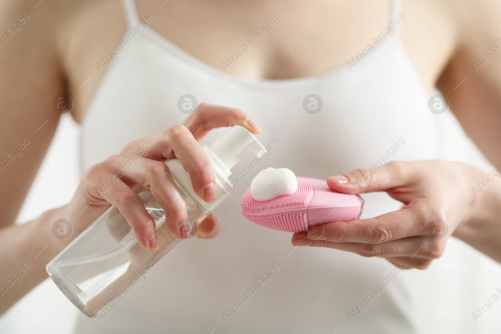 Photo of Washing face. Woman applying cleansing foam onto brush against light background, closeup