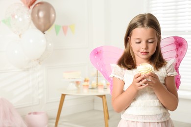 Cute little girl wearing fairy costume with delicious cupcake in decorated room. Space for text