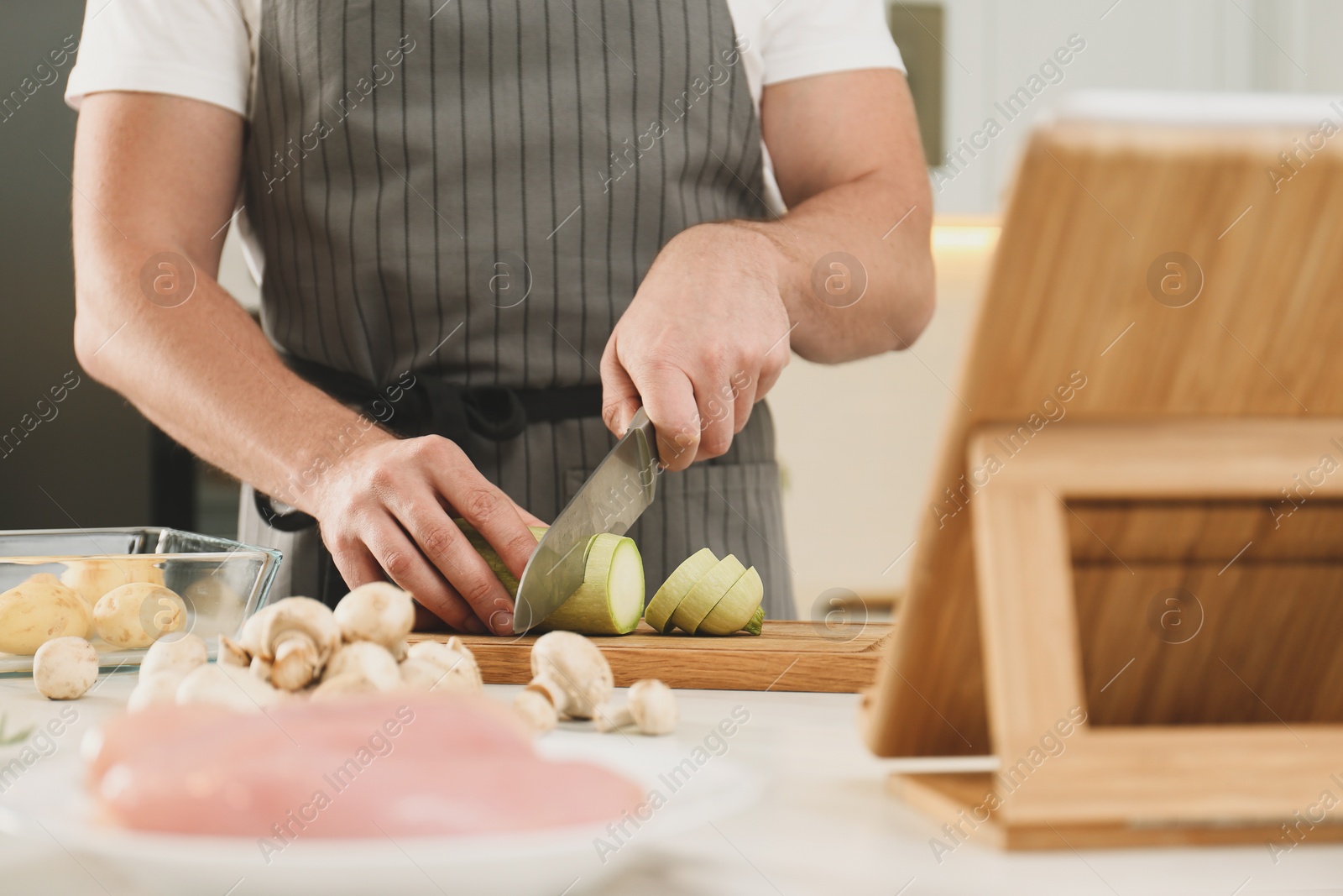 Photo of Man cutting zucchini while watching online cooking course via tablet in kitchen, closeup