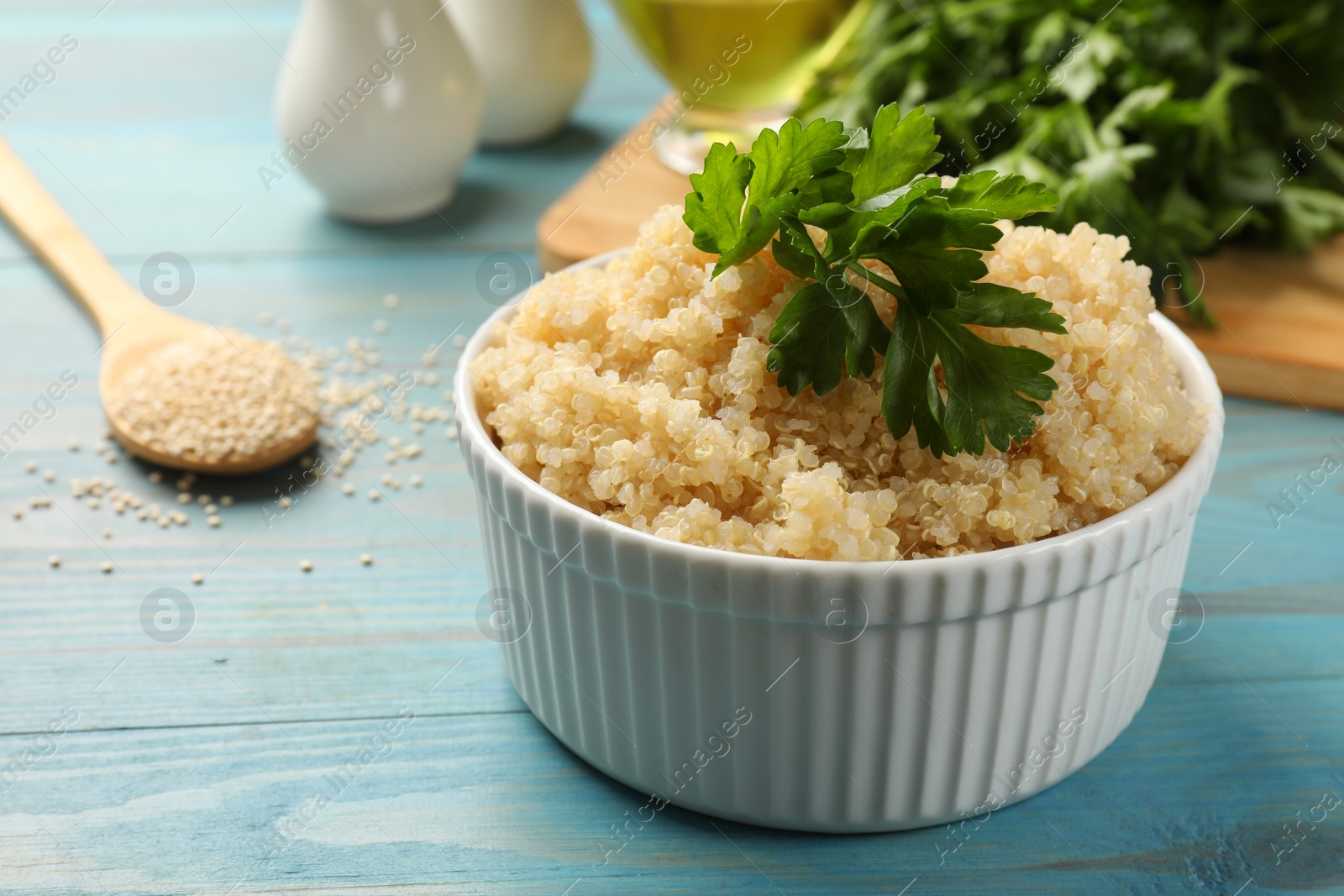 Photo of Tasty quinoa porridge with parsley in bowl on light blue wooden table, closeup. Space for text