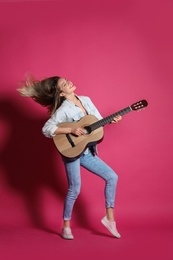 Young woman playing acoustic guitar on color background