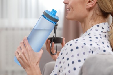 Woman with bottle of water in room, closeup