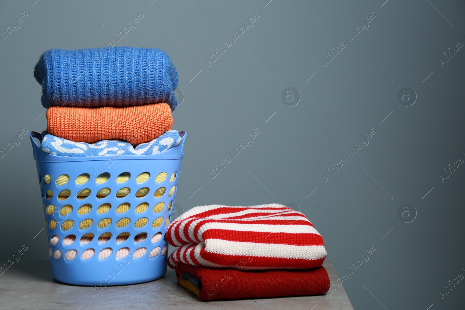 Photo of Plastic laundry basket and clean clothes on grey table. Space for text