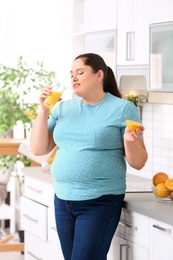 Overweight woman drinking fresh juice and orange in kitchen. Healthy diet