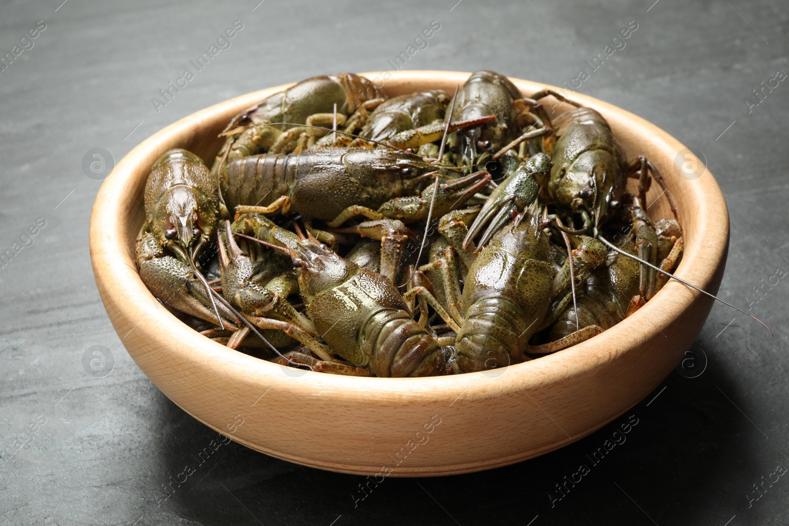 Photo of Fresh raw crayfishes in wooden bowl on black table