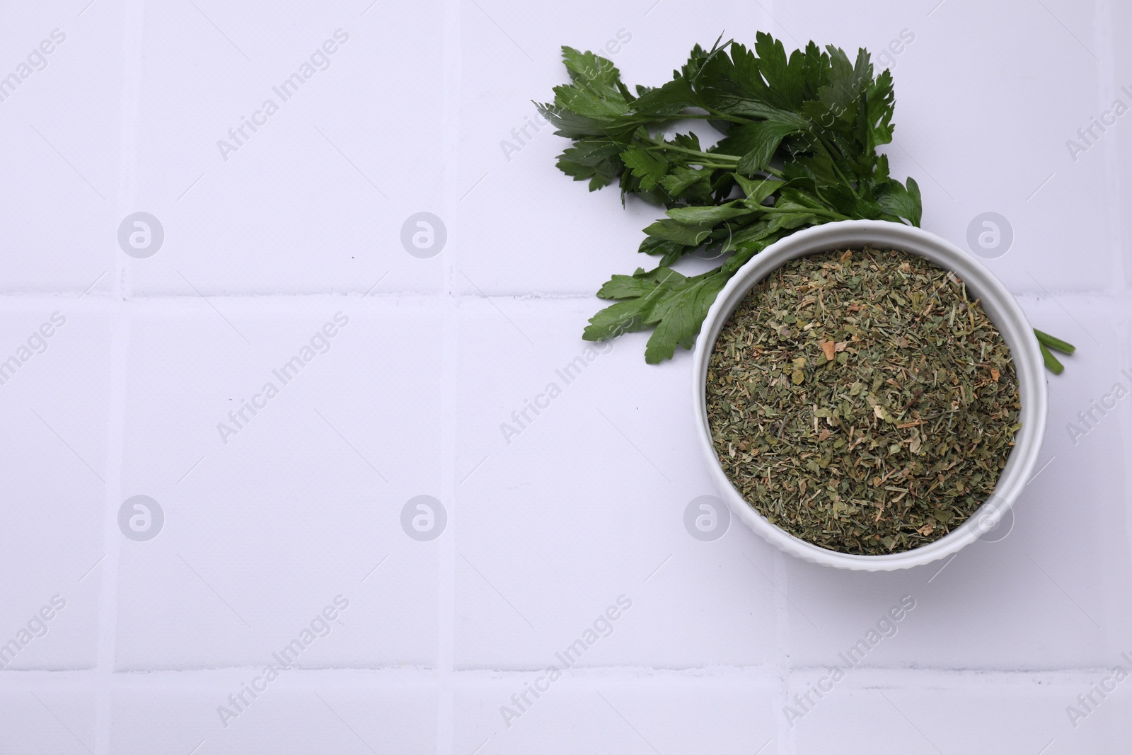 Photo of Dried parsley and fresh leaves on white tiled table, flat lay. Space for text