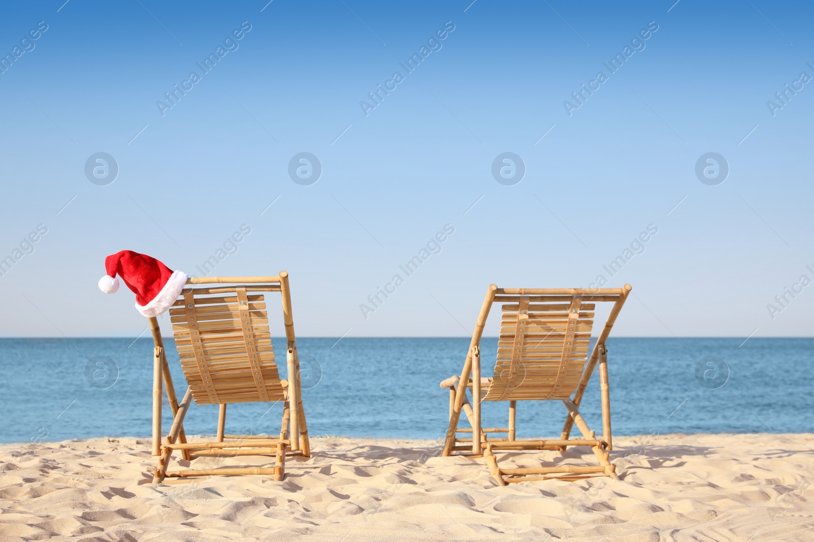 Photo of Sun loungers and Santa's hat on beach, space for text. Christmas vacation