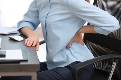 Photo of Young woman suffering from back pain in office, closeup